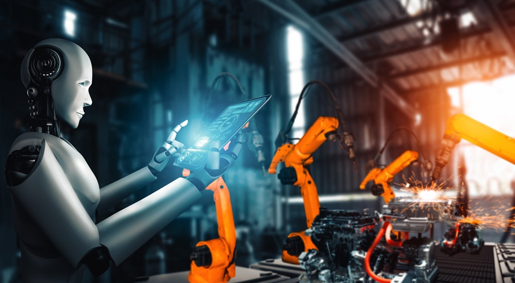 A humanoid robot using a tablet to control robotic arms in an advanced manufacturing facility.