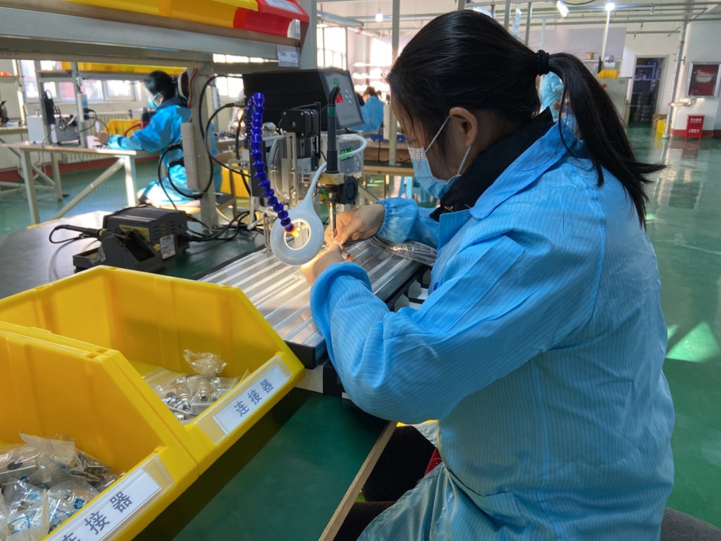 A worker in a blue uniform assembling wire harnesses at a manufacturing station.